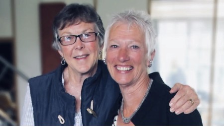 Image shows two women smiling into the camera. One has their arm around the other. 